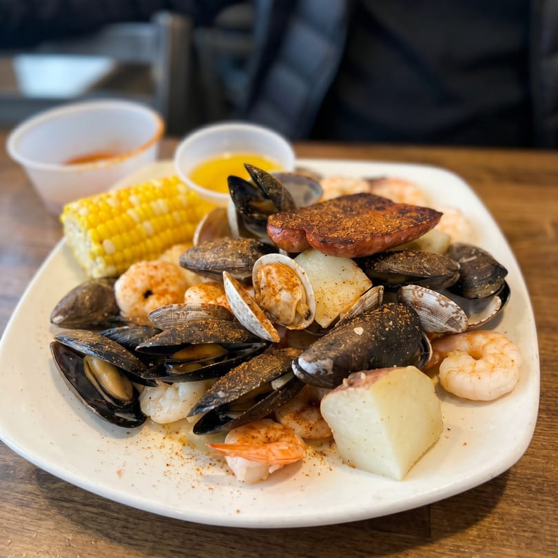 A seafood boil with mussels, clams, shrimp, corn on the cob, and potatoes on a white plate.