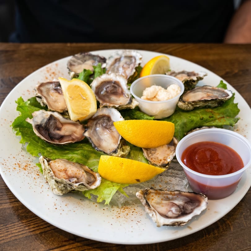 Fresh oysters on the half shell with lemon wedges, cocktail sauce, and horseradish on a white plate.