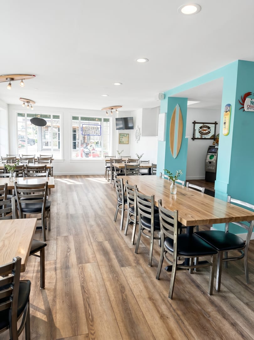 Bright, empty restaurant dining room with wooden tables, black chairs, and a turquoise accent wall.
