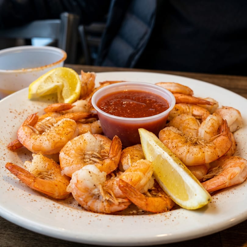 A plate of seasoned shrimp with cocktail sauce and lemon wedges, ready to eat.