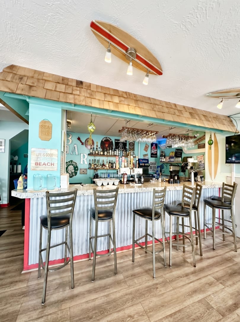 A vibrant bar with a teal wall, corrugated metal counter, and surf-themed decor.